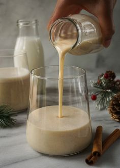 a person pouring milk into a glass with cinnamons and pine cones in the background