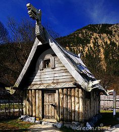 an old wooden shack with a roof made out of logs and wood planks in front of a mountain range