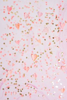 some pink and gold confetti on a white background with lots of hearts in the air