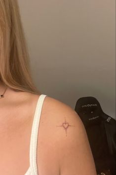 a woman with a small cross tattoo on her left shoulder and right arm behind her back