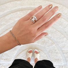 a woman's hand with gold and white nail polish holding a ring on her finger