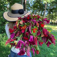 a woman wearing a hat with flowers on her back, in the grass near trees