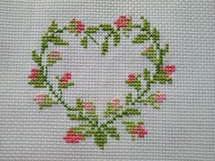 a cross stitch heart with pink flowers and green leaves