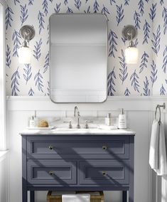 a bathroom with a blue vanity and wallpaper on the walls, along with a large mirror above it