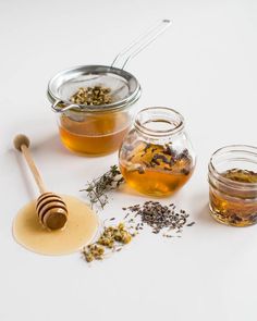 three jars filled with different types of tea and honey on top of a white table