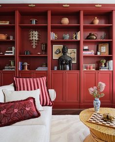 a living room filled with lots of red bookshelves next to a white couch