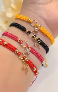 four different bracelets with charms on each arm and one has a cross, two are gold