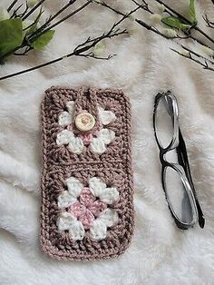 a crocheted cell phone case with flowers on it next to eyeglasses