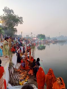 many people are sitting on the bank of a river and some have candles in their hands