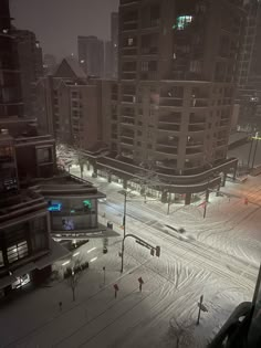 a city street is covered in snow at night with buildings and cars on the road