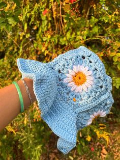 a hand holding up a blue crocheted hat with a flower on the front