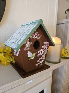 a wooden birdhouse with flowers painted on the side and candles in front of it