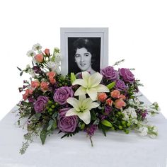 an arrangement of flowers and greenery on a table with a framed photo in the background