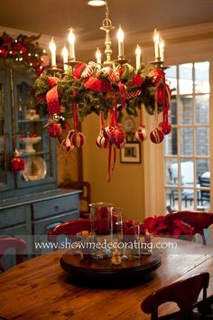 a dining room table decorated for christmas with candles and ornaments hanging from the chandelier