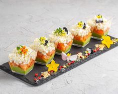 four desserts are arranged in small glass dishes on a black tray with flowers and leaves