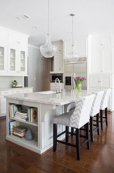 a large kitchen with white cabinets and marble counter tops, along with bar stools