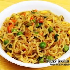 a bowl filled with noodles and vegetables on top of a wooden table next to a fork