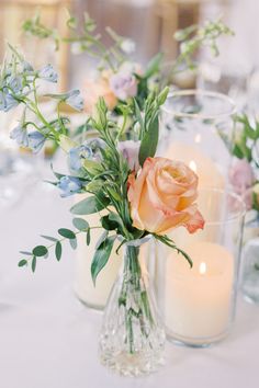 two vases filled with flowers and candles on top of a white tablecloth covered table