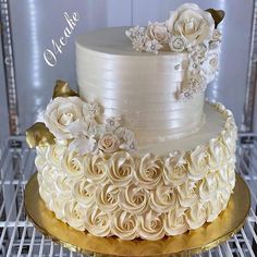 a three tiered cake with white flowers on the top and gold trimmings