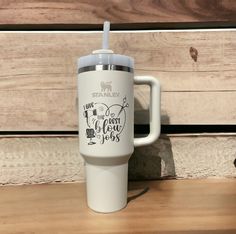 a white travel mug sitting on top of a wooden table next to a cup with a straw in it