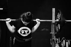 a woman is lifting a barbell with her hands in the air while wearing a black shirt that says gw p y