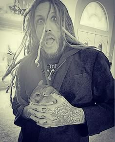 a man with dreadlocks holding a cat in his arms and looking surprised at the camera