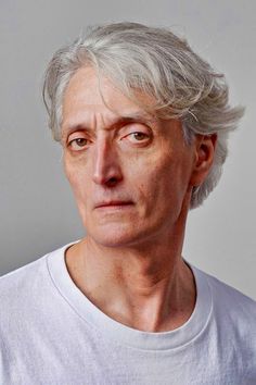 an older man with grey hair and white shirt looking at the camera while wearing a white t - shirt