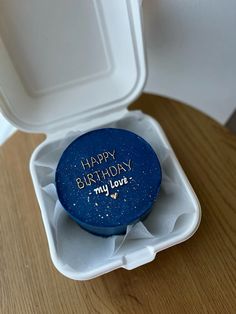 a blue birthday cake in a white box on a wooden table with the lid open