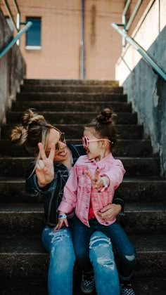 a woman and child sitting on the steps pointing at something in front of them with their fingers up