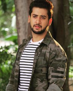 a man with a beard and striped shirt standing in front of some trees looking at the camera