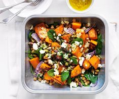 a metal pan filled with vegetables on top of a white table next to utensils