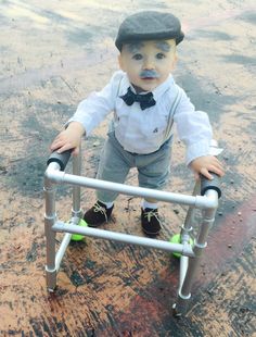 a little boy in a hat and bow tie standing on a metal step ladder with his hands on the handle bars