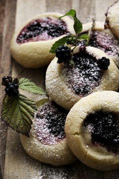 small pastries covered in powdered sugar and blackberries on a wooden cutting board