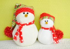 two knitted snowmen sitting next to each other on a white surface with green and yellow background