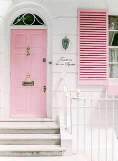 a pink door with shutters on the side of a white building and steps leading up to it