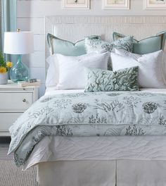 a bed with white and blue comforters in a bedroom next to a lamp on a dresser