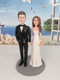 a bride and groom figurine standing next to an open window with seagulls in the background