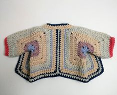 a crocheted jacket is laying on top of a white surface with red, blue and yellow trim