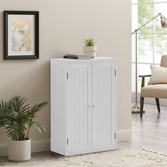 a white cabinet sitting next to a potted plant in a living room on top of a rug