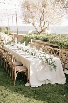 a long table with white flowers and greenery is set up for an outdoor dinner