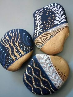 three painted rocks sitting next to each other on top of a gray surface with white and blue designs