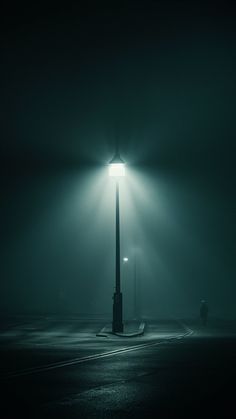 a street light in the middle of a dark parking lot at night with fog on the ground