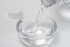 a person pouring water into a glass bowl on a white surface with other items in the background