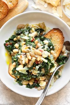 a white bowl filled with beans and spinach on top of a table next to bread