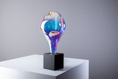 a colorful glass object sitting on top of a black stand in front of a gray wall