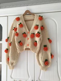 a knitted sweater with orange roses on it hanging from a white coat hanger