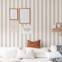 a living room with striped wallpaper and white couch in the foreground, framed pictures on the wall