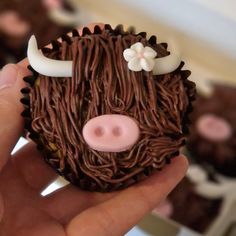 a hand holding a chocolate cupcake decorated to look like a cow's head