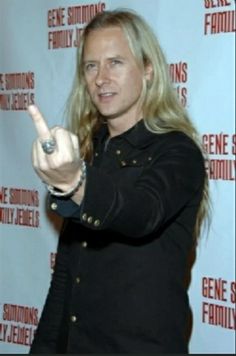 a man with long hair pointing to the side while wearing a black shirt and jeans