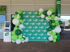 a green and white balloon arch on display in front of a building with an atm machine